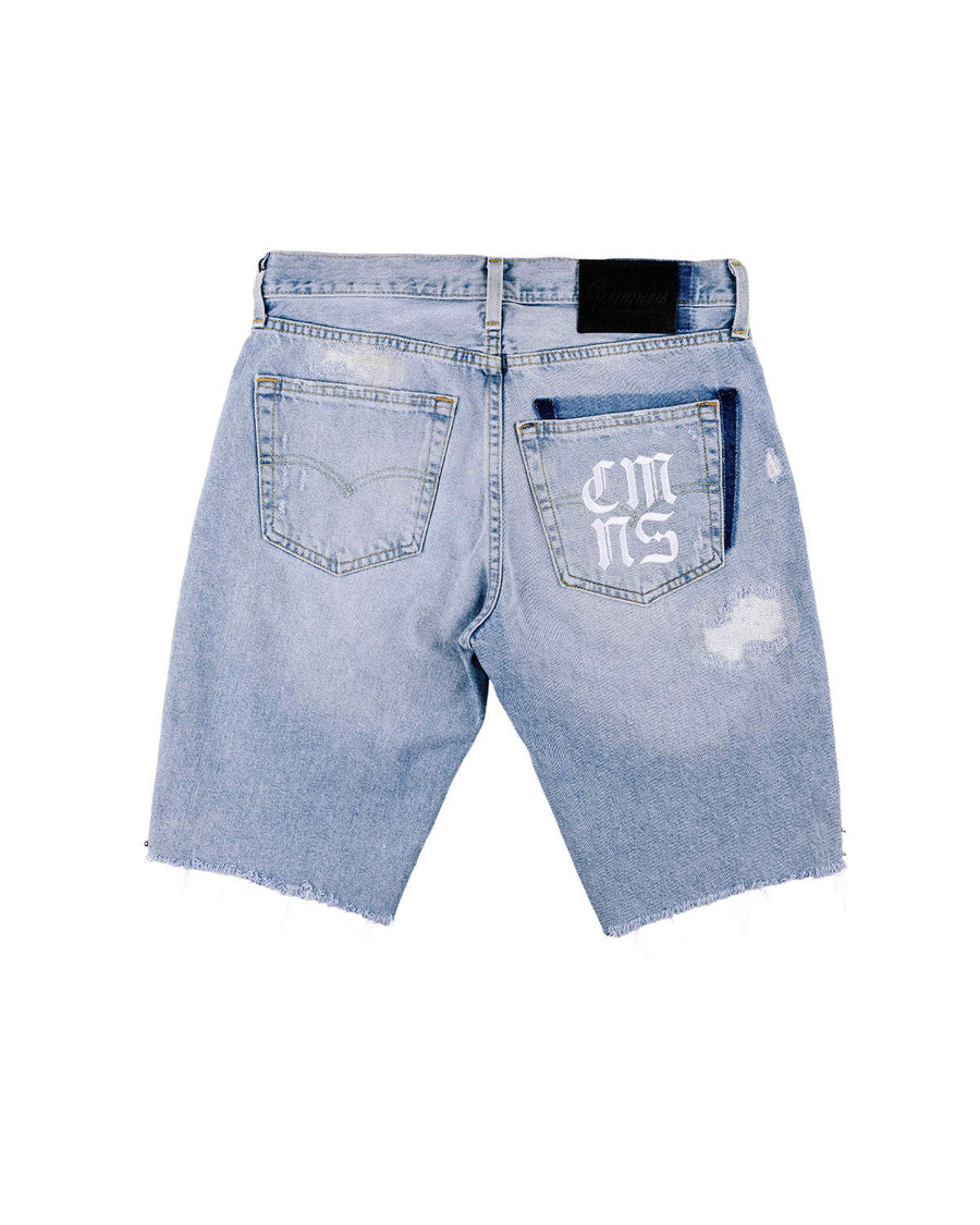 Back view of light blue denim shorts with raw hems, distressed patches, and white lettering on the right back pocket.