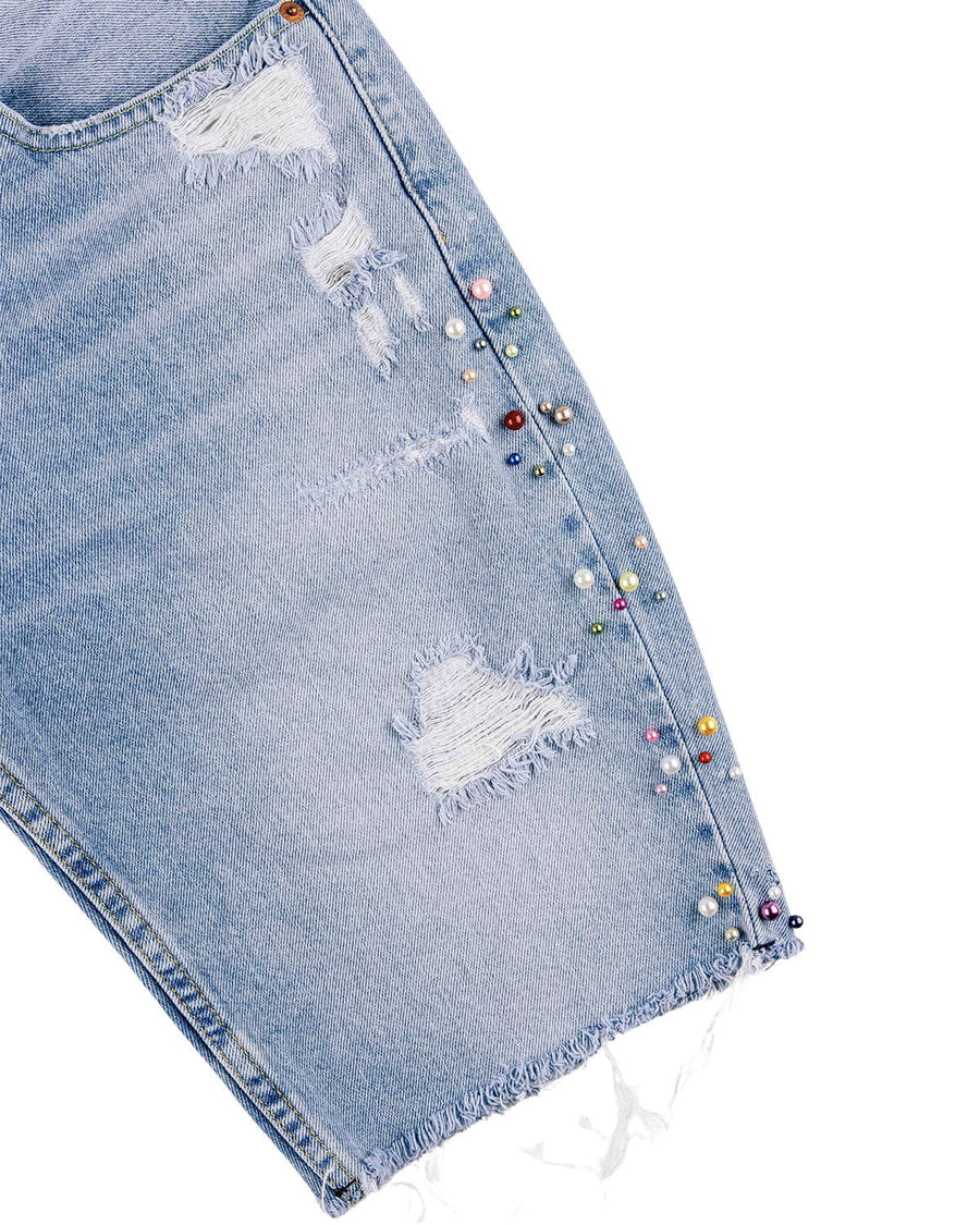Light blue denim shorts with distressed patches, a frayed hem, and multicolored pearl-like beads along the side seam.