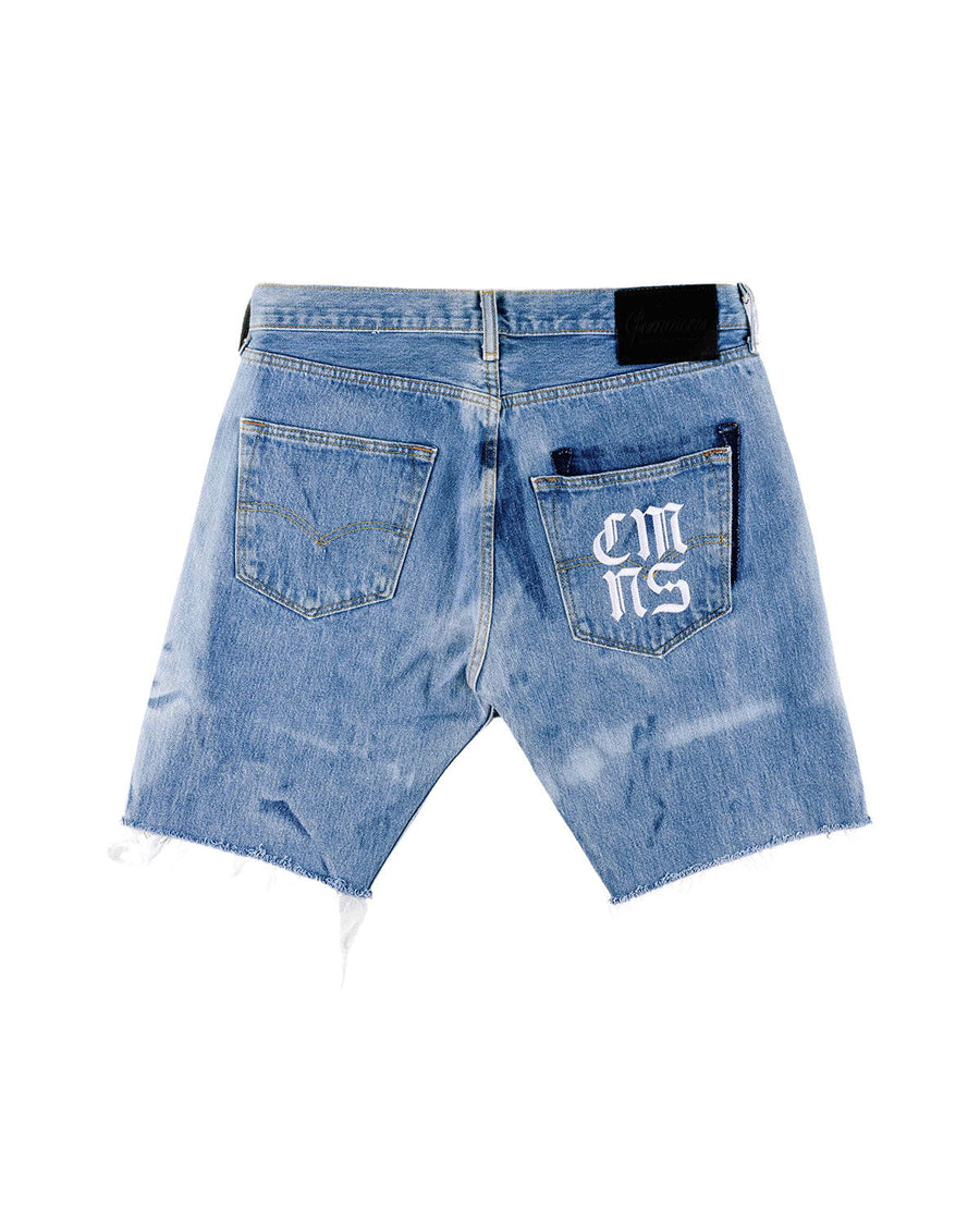 Back view of light blue denim shorts with frayed hems, two pockets, white lettering and a black waistband patch.