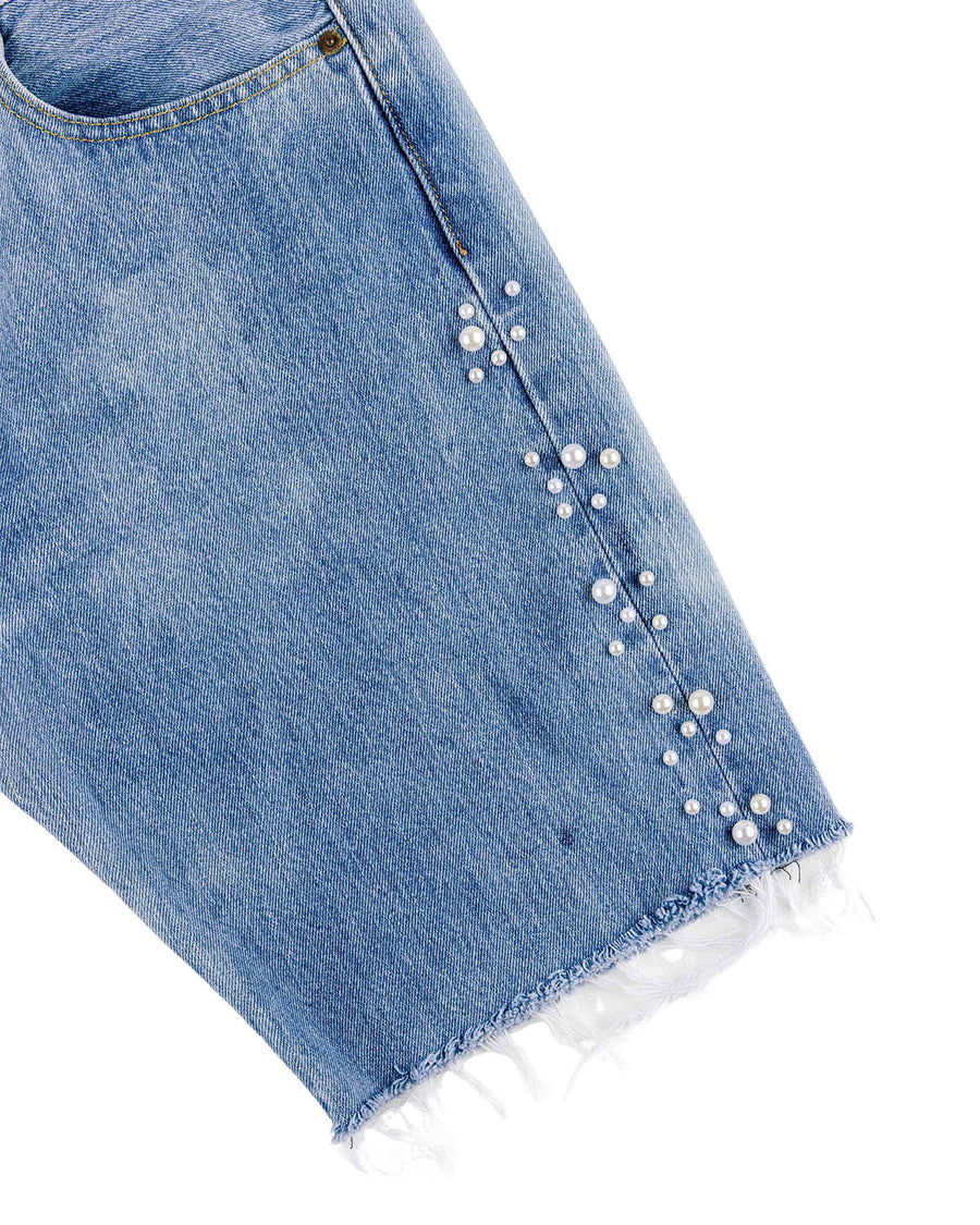 Close-up of light blue denim shorts with white pearl embellishments along the side seam and a frayed hem.