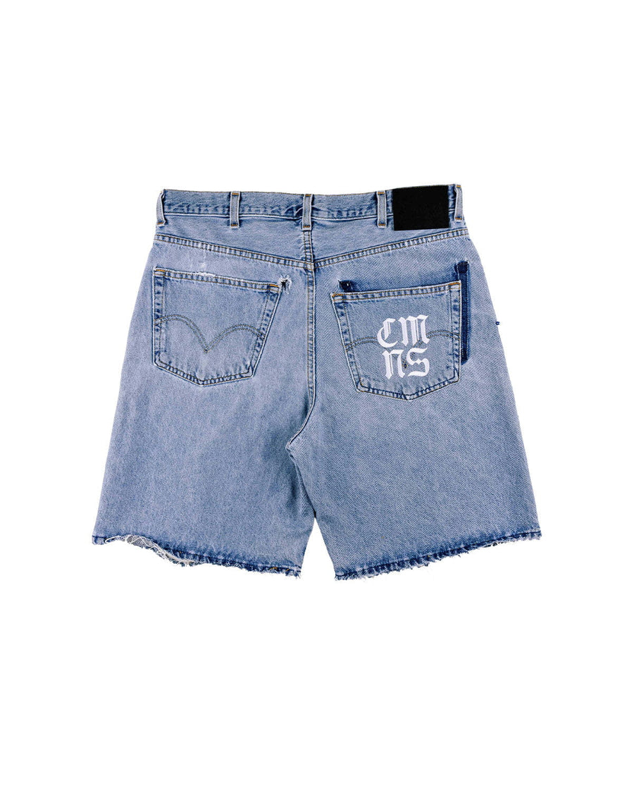 Back view of light blue denim shorts with frayed hems, two pockets, white pocket lettering, and a black waistband patch.