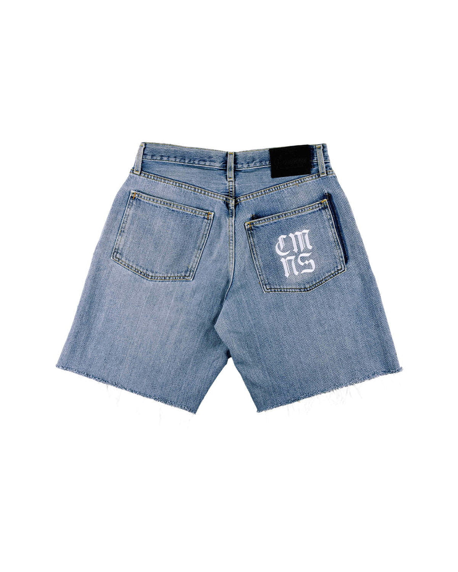 Back view of light blue denim shorts with raw hems, two pockets, a white pocket monogram, and a black waistband patch.