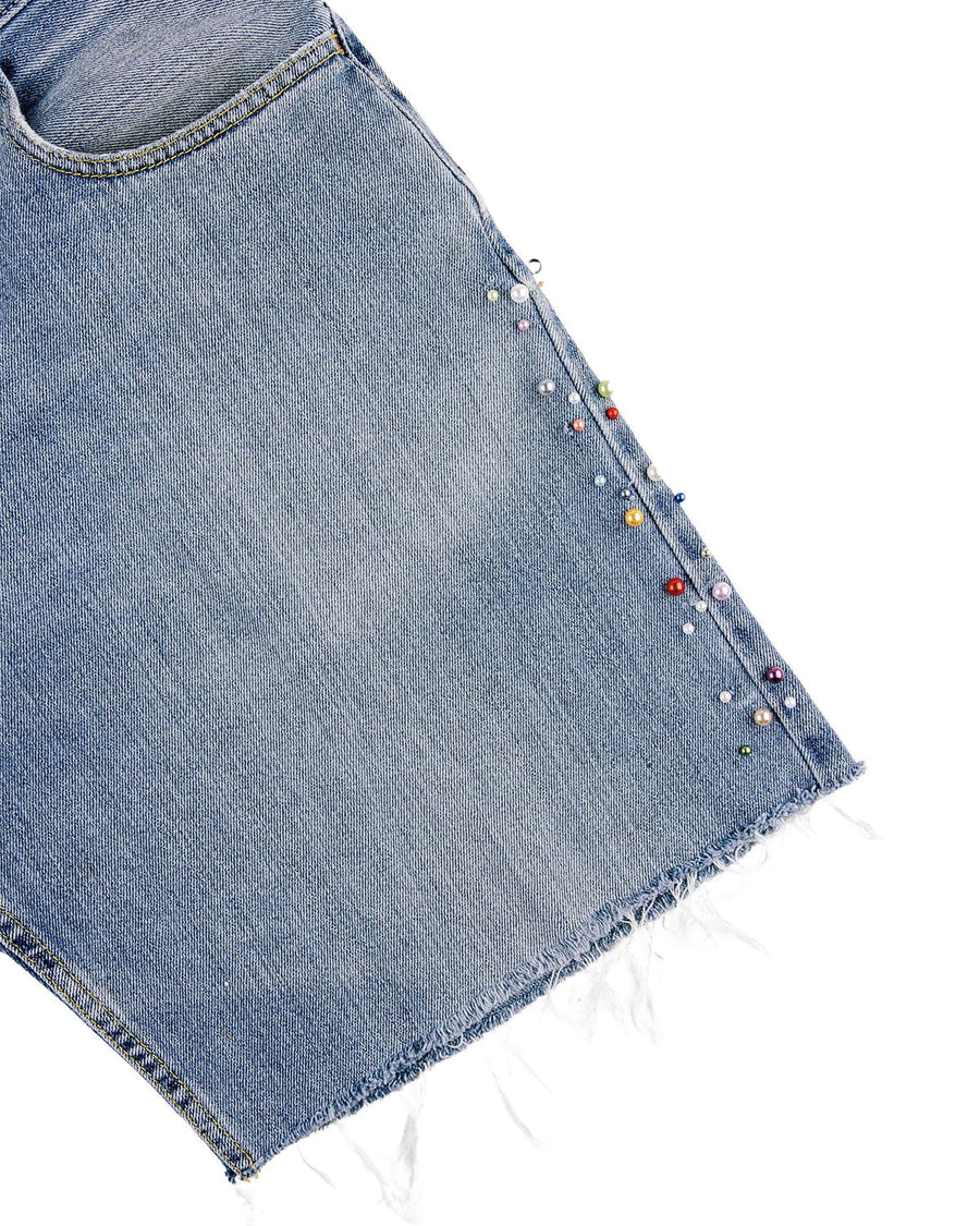 Close-up of light blue denim shorts with a front pocket, multicolored pearl-like beads along the seam, and a frayed hem.