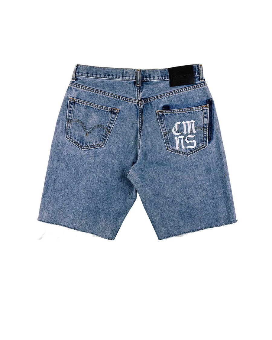 Back view of blue denim shorts with raw hems, two pockets, white lettering on the right pocket, and a black waistband patch.