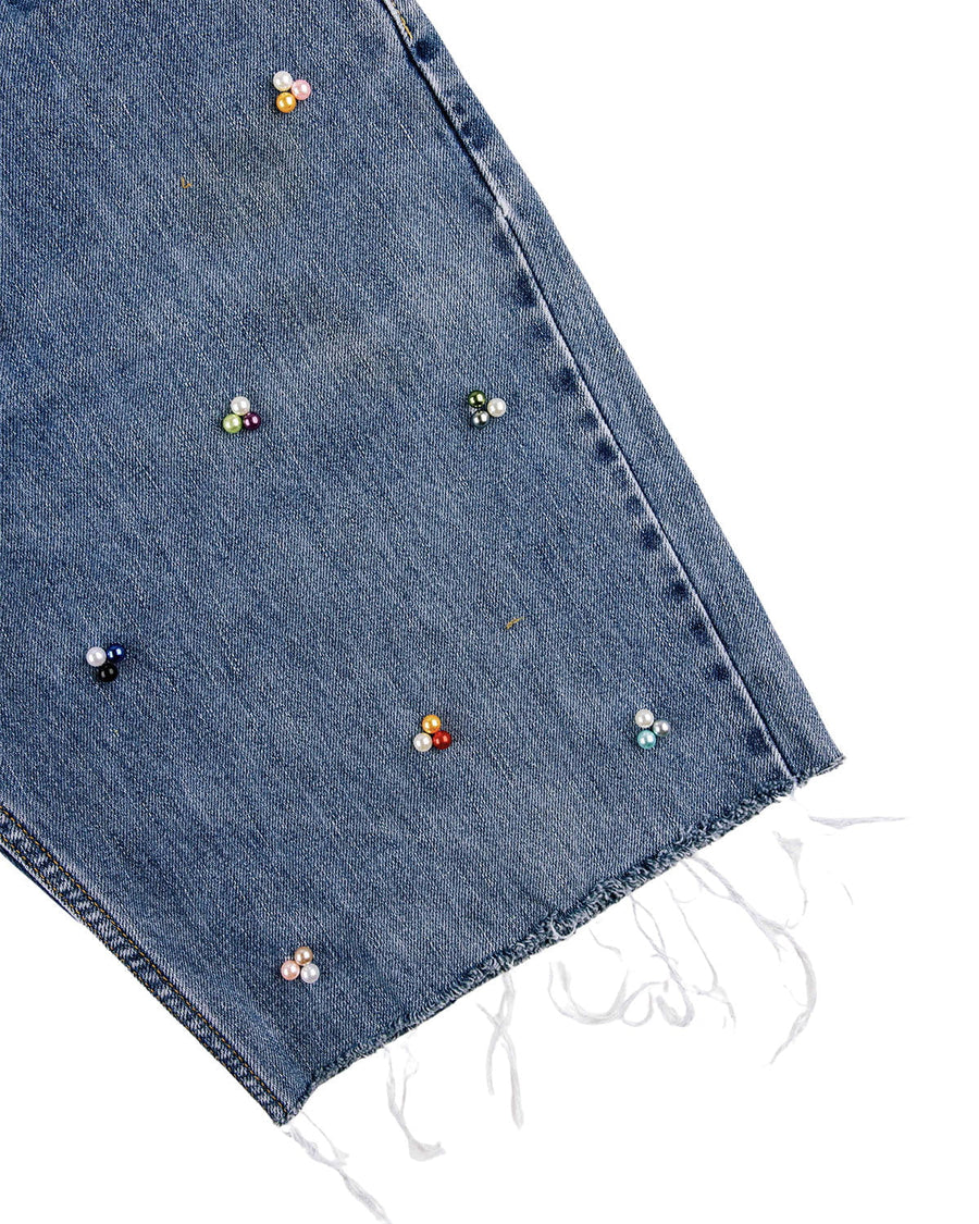 Close-up of a blue denim pant leg with multicolored pearl-like bead clusters and a frayed hem on a white background.