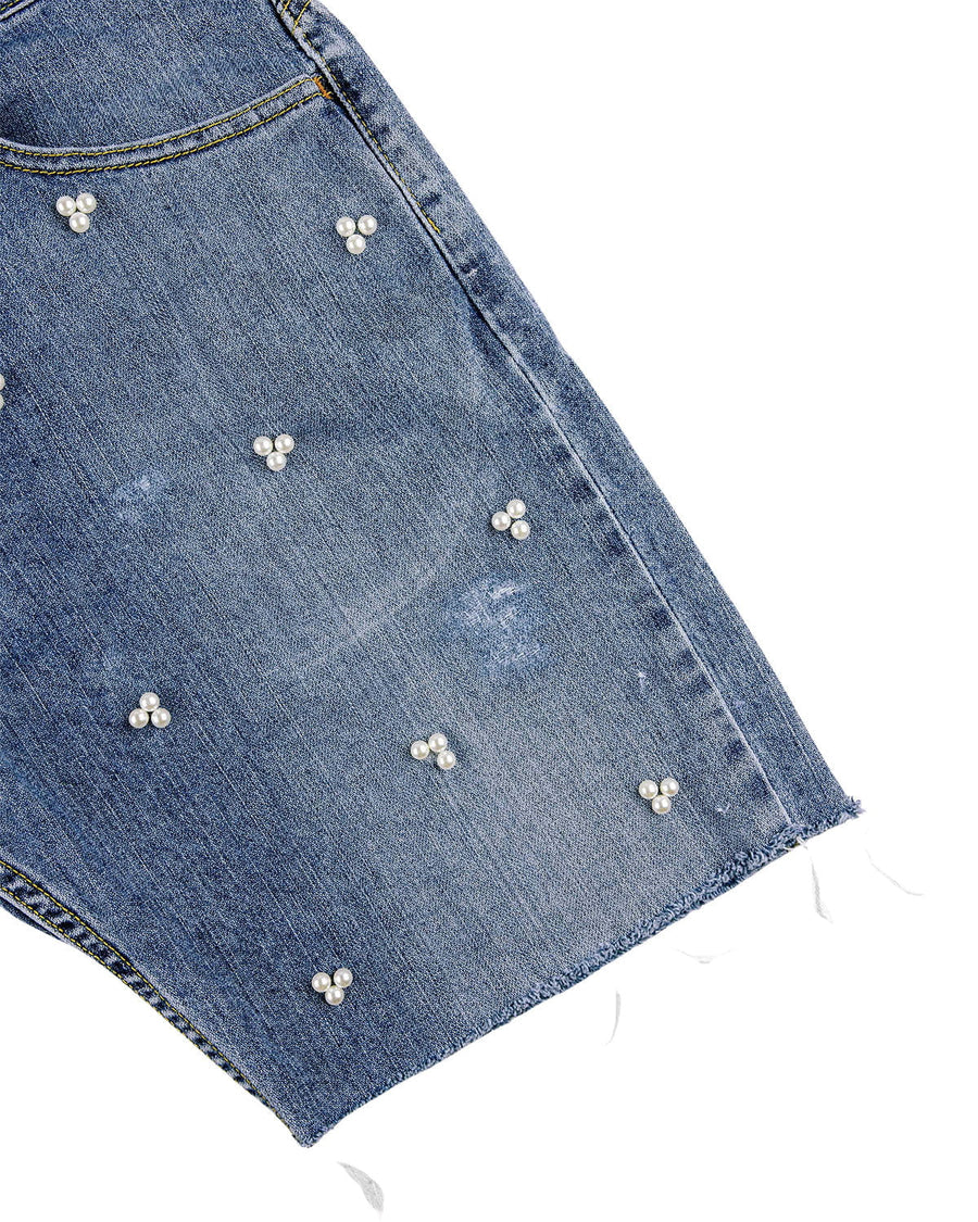 Close-up of blue denim shorts with white pearl bead clusters, faded details, a front pocket and a raw hem.