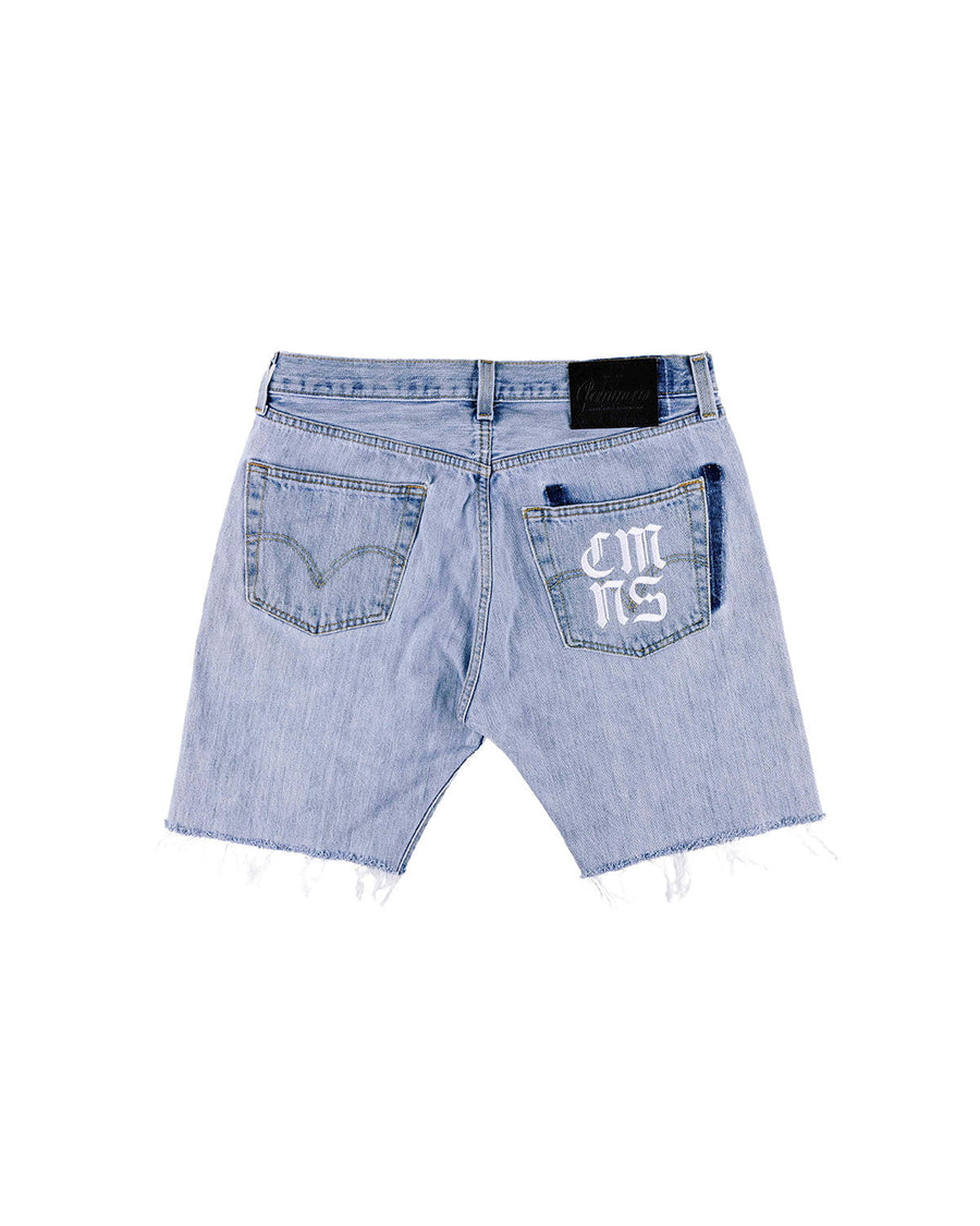 Back of light blue denim shorts with frayed hems, two pockets, white pocket lettering, and a black waistband patch.
