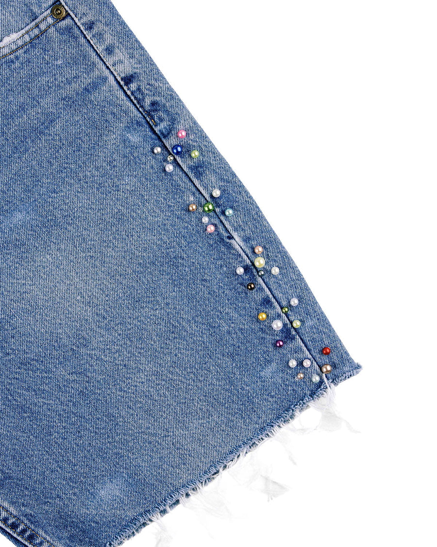 Blue denim skirt detail with multicolored pearl-like beads along the side seam and a frayed hem on white.