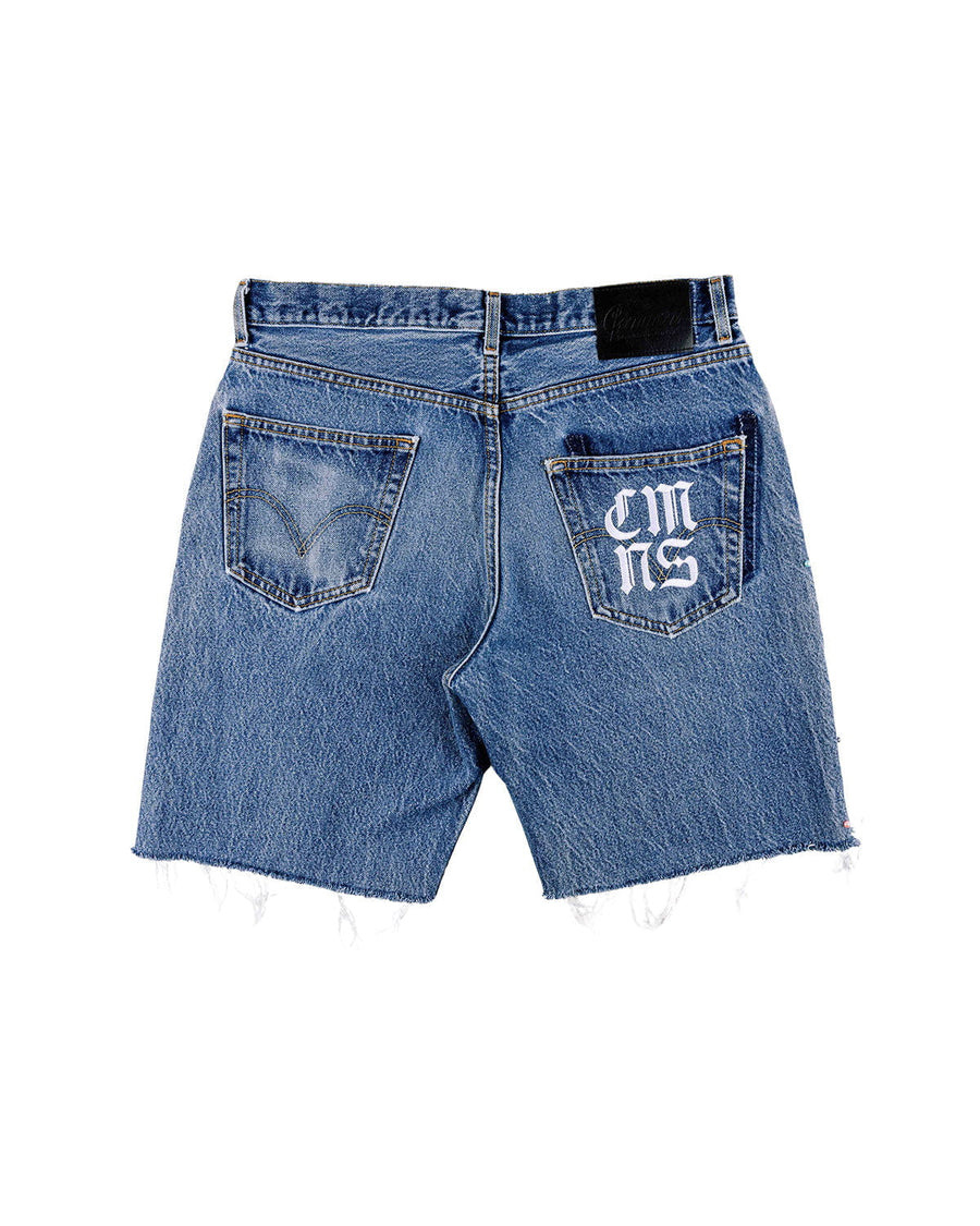 Back view of blue denim shorts with frayed hems, two pockets, white lettering on one pocket, and a black waistband patch.