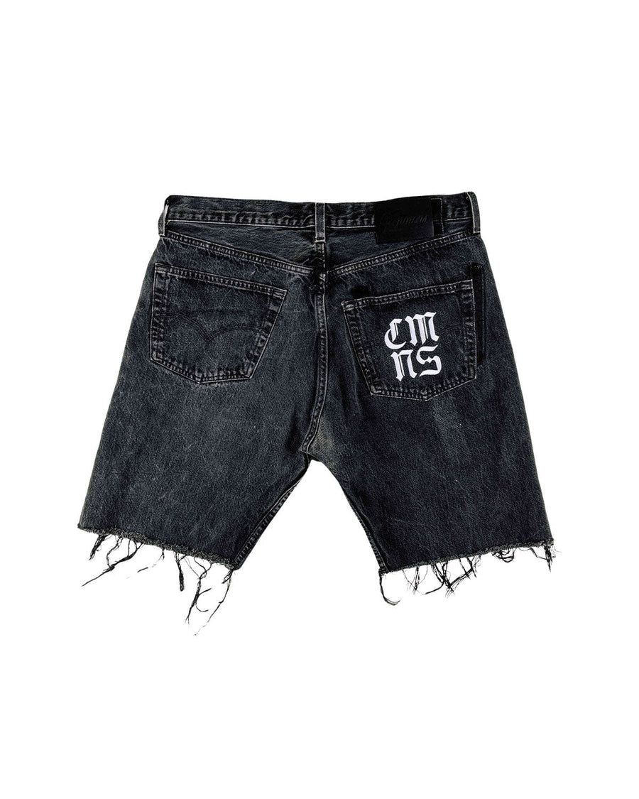 Back view of washed black denim shorts with frayed hems, two back pockets, and white lettering on the right pocket.