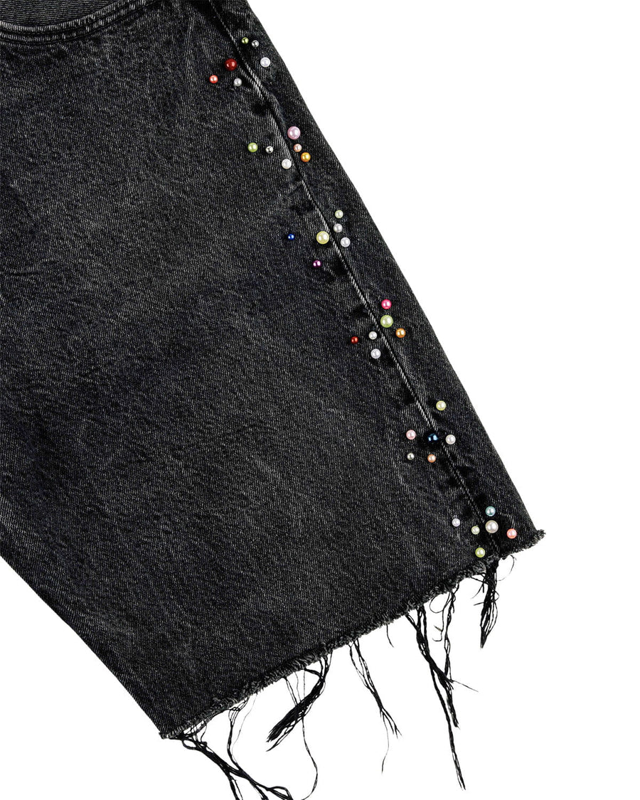 Close-up of black denim shorts with multicolored pearl-like beads along the side seam and a frayed hem on white.