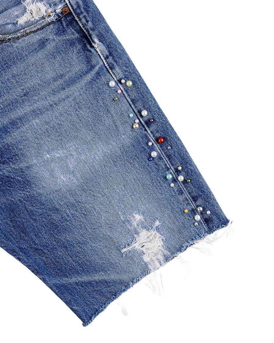 Distressed blue denim shorts with a frayed hem and multicolored pearl-like beads along the side seam on white.
