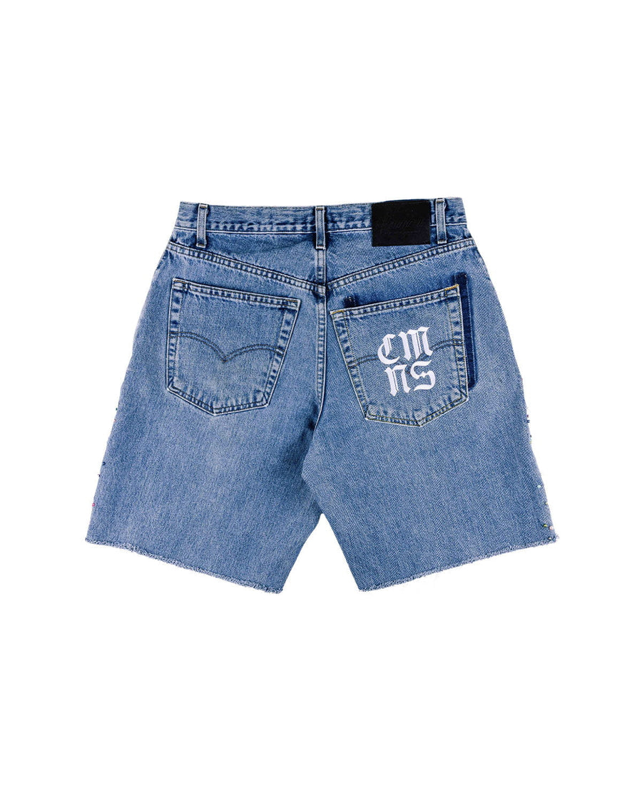 Back view of blue denim shorts with raw hems, two pockets, white lettering on one pocket, and a black waistband patch.
