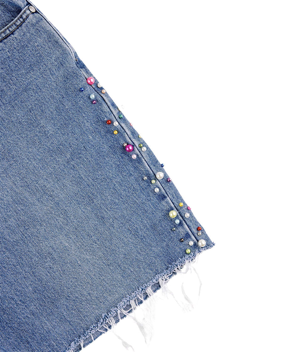 Blue denim skirt detail with multicolored pearl-like beads along the side seam and a frayed hem on white.
