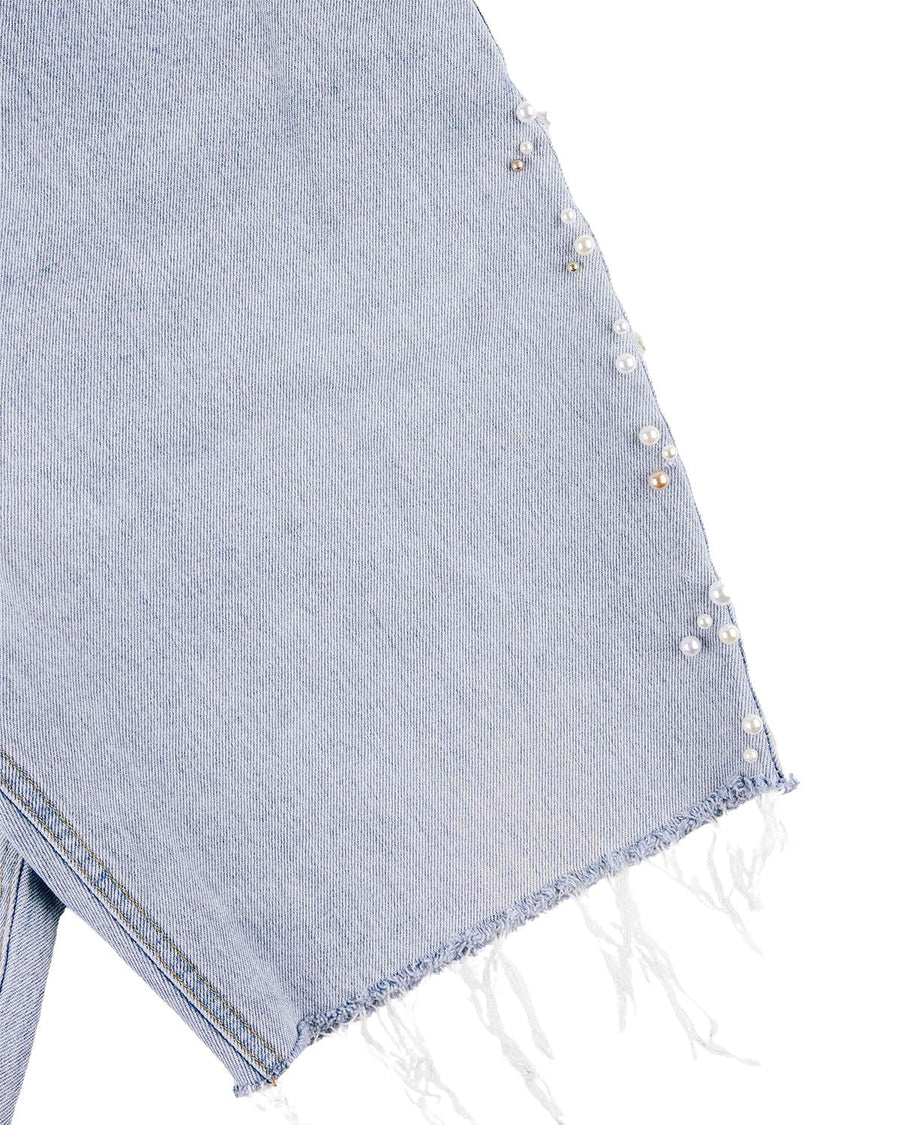 Close-up of light blue denim with pearl-like beads along the side and a frayed raw hem against a white background.