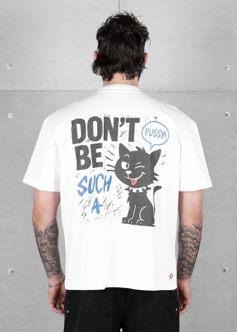 Back view of a model wearing a white T-shirt with a black cartoon cat and blue and black lettering against a concrete wall.