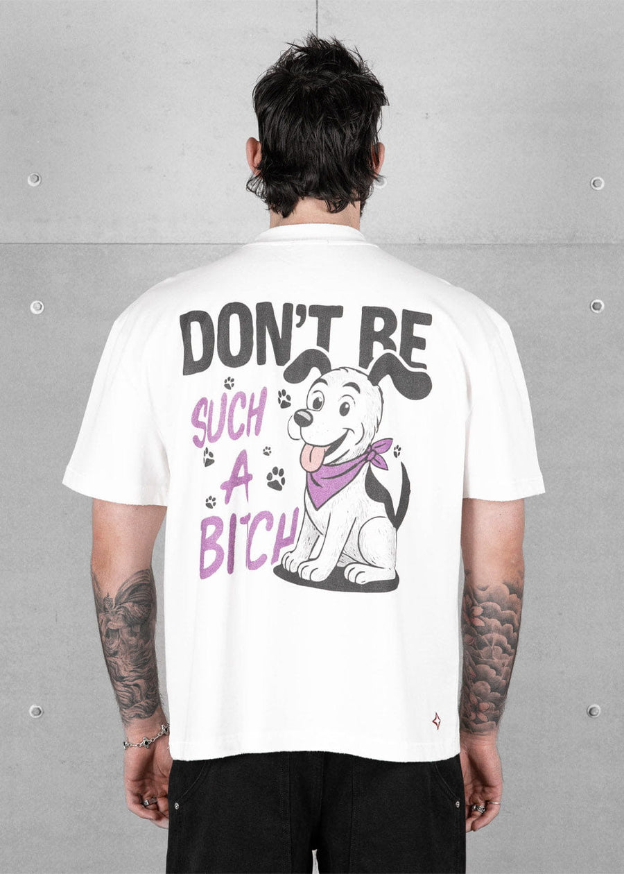 Back view of a model wearing a white T-shirt with a cartoon puppy and black and purple lettering against a concrete wall.