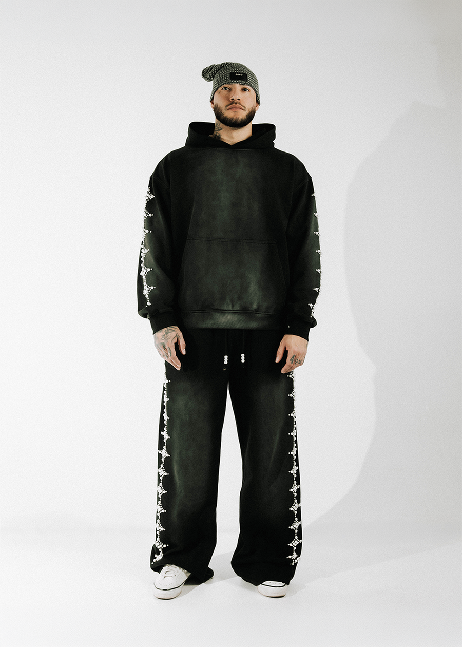 Model wearing a washed black hoodie and wide-leg sweatpants with white bead trim, a knit beanie, and white sneakers.