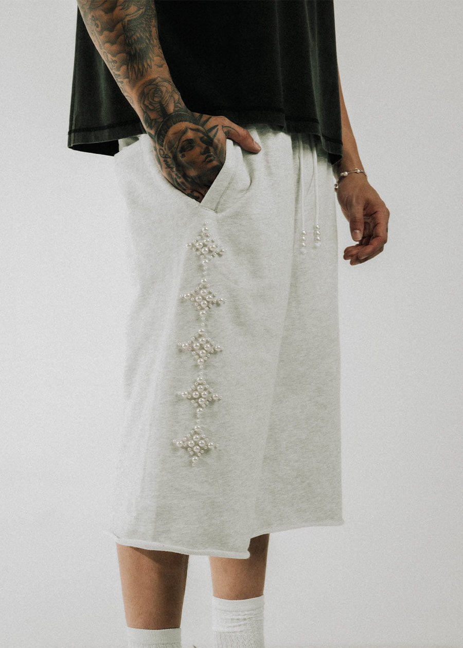 Light gray knit shorts with pearl diamond motifs, side pockets, and beaded drawstrings, worn with a black shirt.